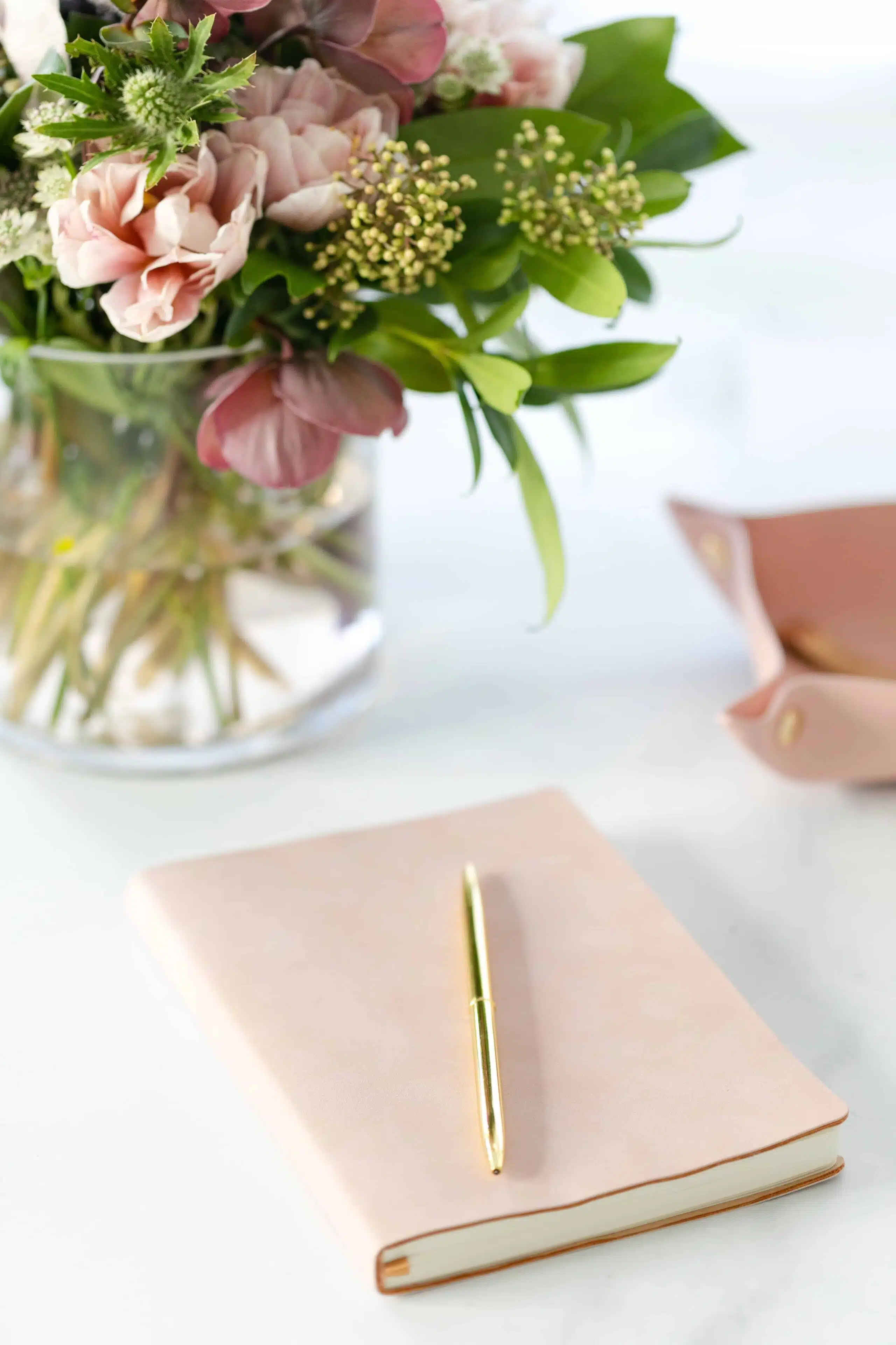 Notitieboek en pen naast een boeket bloemen op een bureau